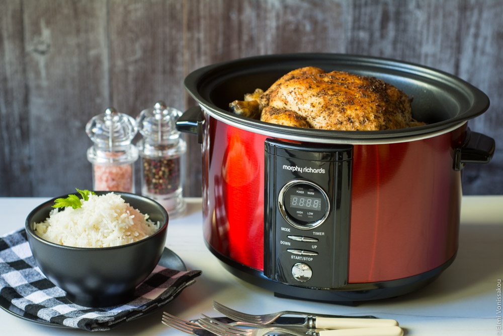 Βιβλίο Μαγειρικής Ελληνικές Συνταγές για Slow Cooker και Διαγωνισμός Giveaway www.thefoodiecorner.gr Photo description: Side view of a small slow cooker on a table with the top of a whole cooked chicken visible. To the side of the cooker is a small bowl of rice and salt and pepper mills.