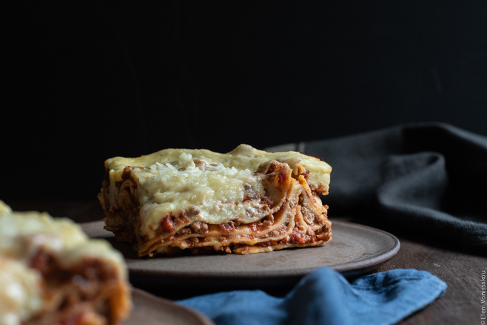 Slow Cooker Lasagna with Meat Sauce and Béchamel www.thefoodiecorner.gr Photo description: A side view of a piece of lasagna, the layers clearly visible with meat sauce and béchamel in between. 