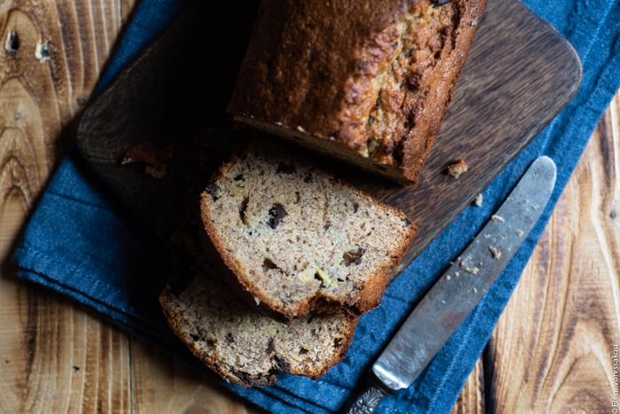 Chocolate Chip Emmer Flour Banana Bread with Tahini www.thefoodiecorner.gr Photo description: A couple of pieces of banana bread lying on a chopping board, in front of the banana bread loaf (half visible). Next to the pieces is a vintage knife. The chopping board is sitting on a folded tea towel.