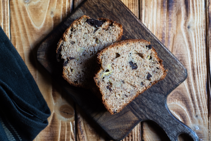 Chocolate Chip Emmer Flour Banana Bread with Tahini www.thefoodiecorner.gr Photo description: A close view of two pieces of banana bread, lying on their side on a wooden chopping board.