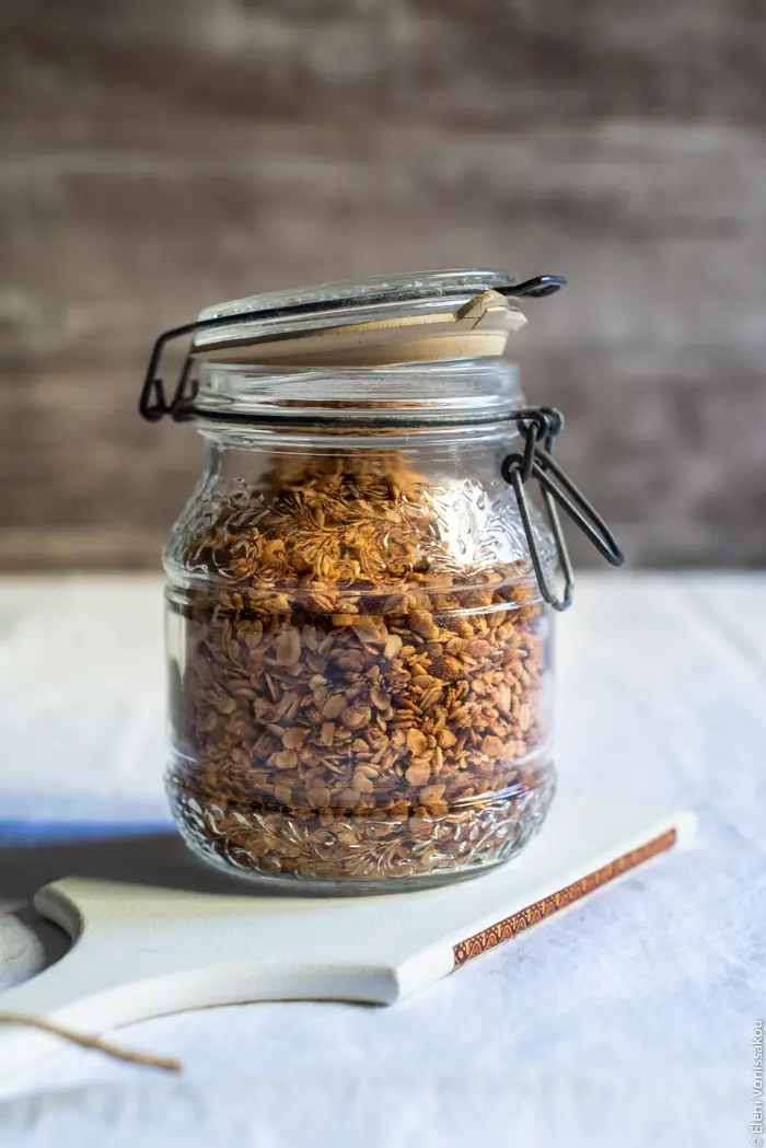 Slow Cooker Peanut Butter Granola with Pure Sesame Oil and Honey www.thefoodiecorner.gr Photo description: A side view of a mason jar with granola inside, sitting on a small white chopping board.