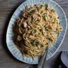 Quick and Easy Smoked Tuna Spaghetti with Parsley and Capers www.thefoodiecorner.gr Photo description: A pretty, handmade ceramic platter full of smoked tuna spaghetti, on a wooden surface. On the platter to the side of the spaghetti are two forks. In the bottom right corner of the photo is a bunched up linen napkin.