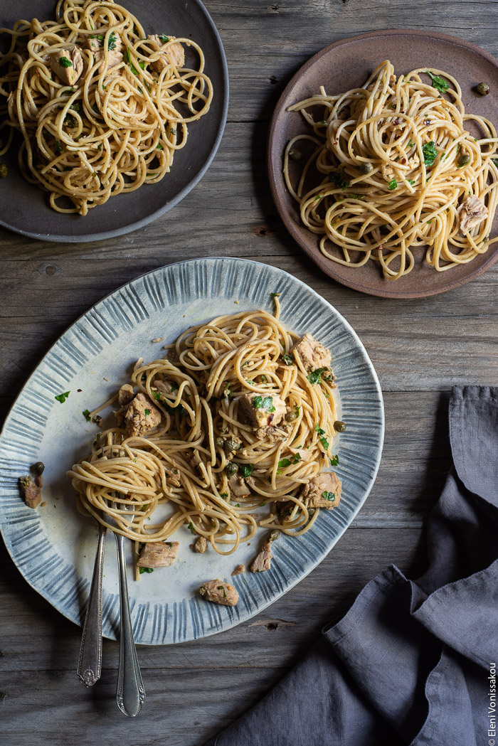 Quick and Easy Smoked Tuna Spaghetti with Parsley and Capers www.thefoodiecorner.gr Photo description: A ceramic platter with some smoked tuna pasta and a couple of serving forks on it. To the top of the platter are two ceramic plates also containing smoked tuna pasta. To the bottom right of the photo is a bunched up linen napkin.