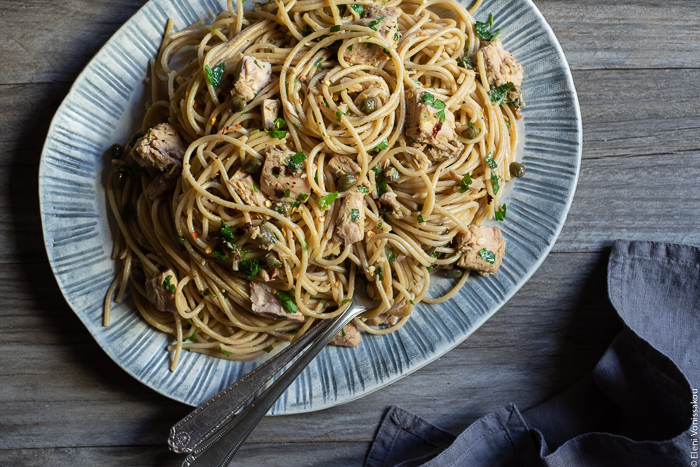 Quick and Easy Smoked Tuna Spaghetti with Parsley and Capers www.thefoodiecorner.gr Photo description: A close up of a ceramic platter full of smoked tuna pasta, with the tuna, capers and parsley visible among the spaghetti. Two serving forks lie half-burried in the pasta. To the bottom right is a bunched up linen napkin.