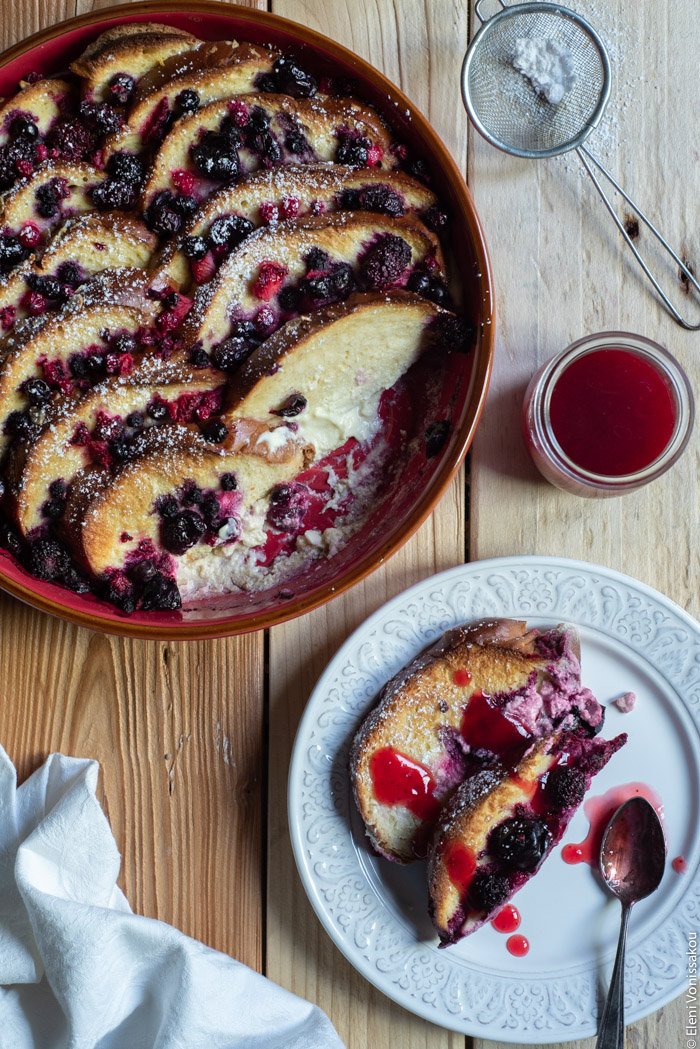 Lemon Berry Tsoureki (Greek Sweet Bread) Pudding www.thefoodiecorner.gr Photo description: A baking dish full of tsoureki pudding, with a couple of slices missing from one side. Below the dish is a plate with some pudding on it, drizzled with fruit sauce. 