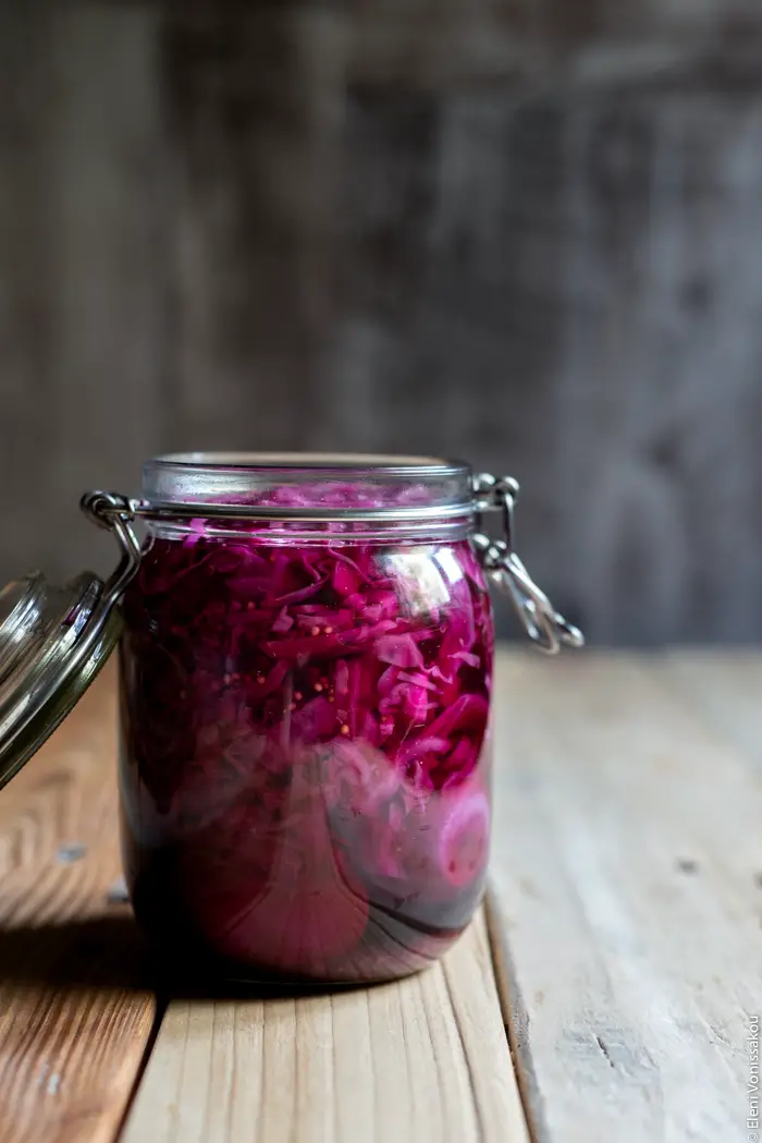 Αυγά και Κόκκινο Λάχανο Τουρσί www.thefoodiecorner.gr Photo description: A side view of a jar with purple pickling liquid inside. Some red cabbage is visible within the liquid.