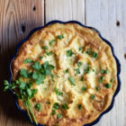 Shepherd’s Pie. To use up those Easter lamb leftovers. www.thefoodiecorner.gr Photo description: An overhead view of a shepherd’s pie in a baking dish with a pretty flowery-shaped rim. The dish is on a wooden surface. The top of the pie is decorated with some chopped parsley and a couple of whole sprigs on the side.