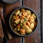 Slow Cooker Sweet Potato Chickpea Coconut Curry www.thefoodiecorner.gr Photo description: A large ceramic bowl with sweet potato chickpea coconut curry sitting on a wooden surface. To the top of the photo, barely visible is a bowl of basmati and wild rice. To the left of the curry are some wooden serving utensils and to the bottom is a bunched up tea towel.