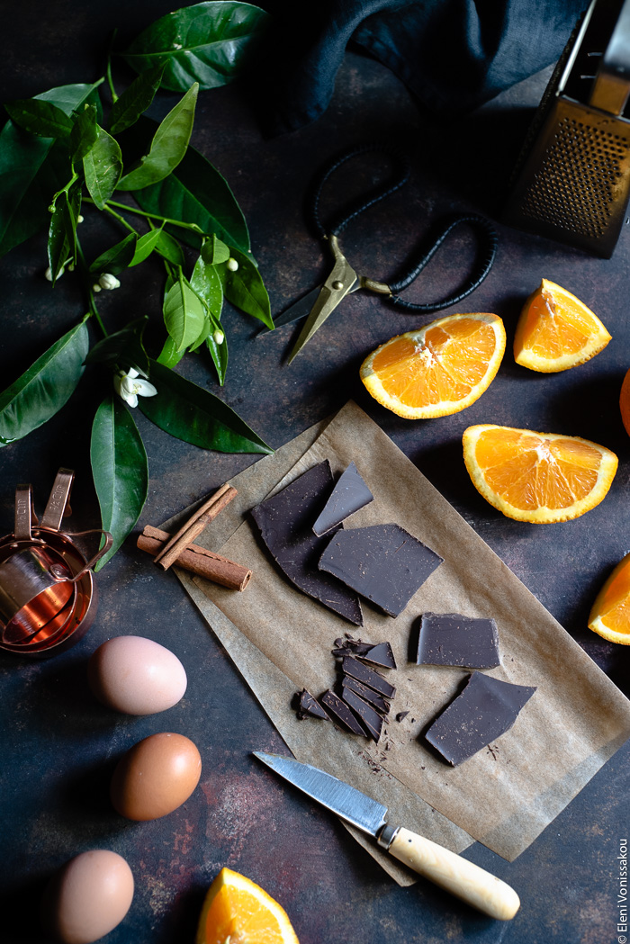 Chocolate Orange Curd – The Easy Way www.thefoodiecorner.gr Photo description: Top view of some ingredients on a dark surface. Some pieces of orange to the right, some pieces of chocolate on grease-proof paper in the centre, eggs to the left and some orange leaves with blossoms at the top of the image.