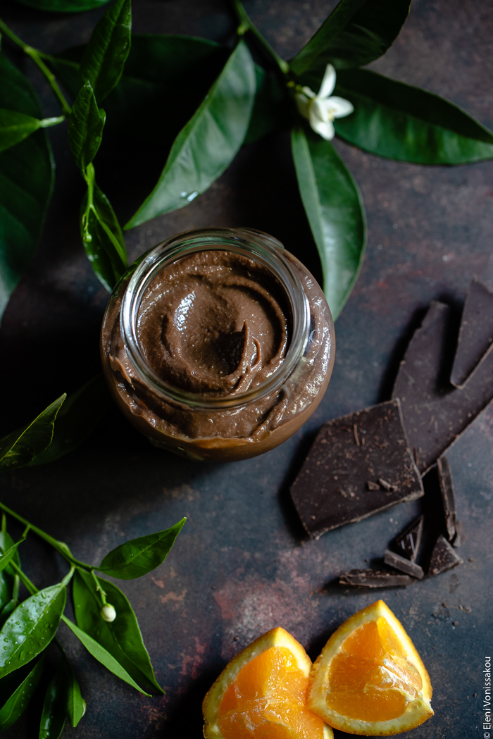 Chocolate Orange Curd – The Easy Way www.thefoodiecorner.gr Photo description: An overhead view of a jar of chocolate orange curd without its lid. To the top of the jar are some orange leaves and blossoms, to the bottom some pieces of chocolate and some pieces of orange.