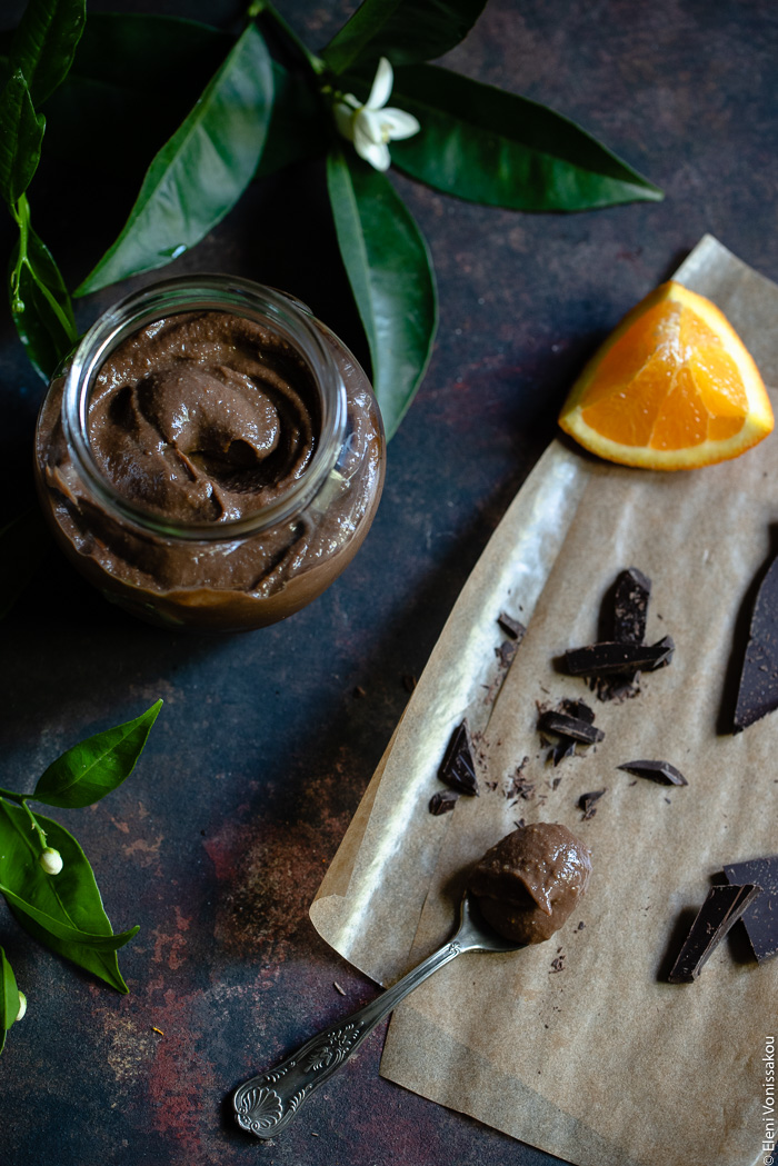 Chocolate Orange Curd – The Easy Way www.thefoodiecorner.gr Photo description: An open jar of chocolate orange curd in the top left corner, next to some orange leaves. To the right are some pieces of chocolate and orange, lying on grease-proof paper. Among the pieces is a spoon full of curd.