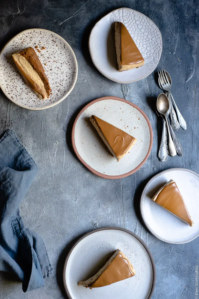 Easy Speculoos Cheesecake www.thefoodiecorner.gr Photo description: five ceramic plates each with a slice of cheesecake. Some spoons to the right of the image and a linen tea towel to the left, half visible.