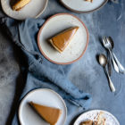 Easy Speculoos Cheesecake www.thefoodiecorner.gr Photo description: five plates each with a slice of speculoos cheesecake. A couple of slices have fallen on their side and one plate has a spoon with a bite of cheesecake on it. Three of the plates are sitting on a bunched up linen tea towel.