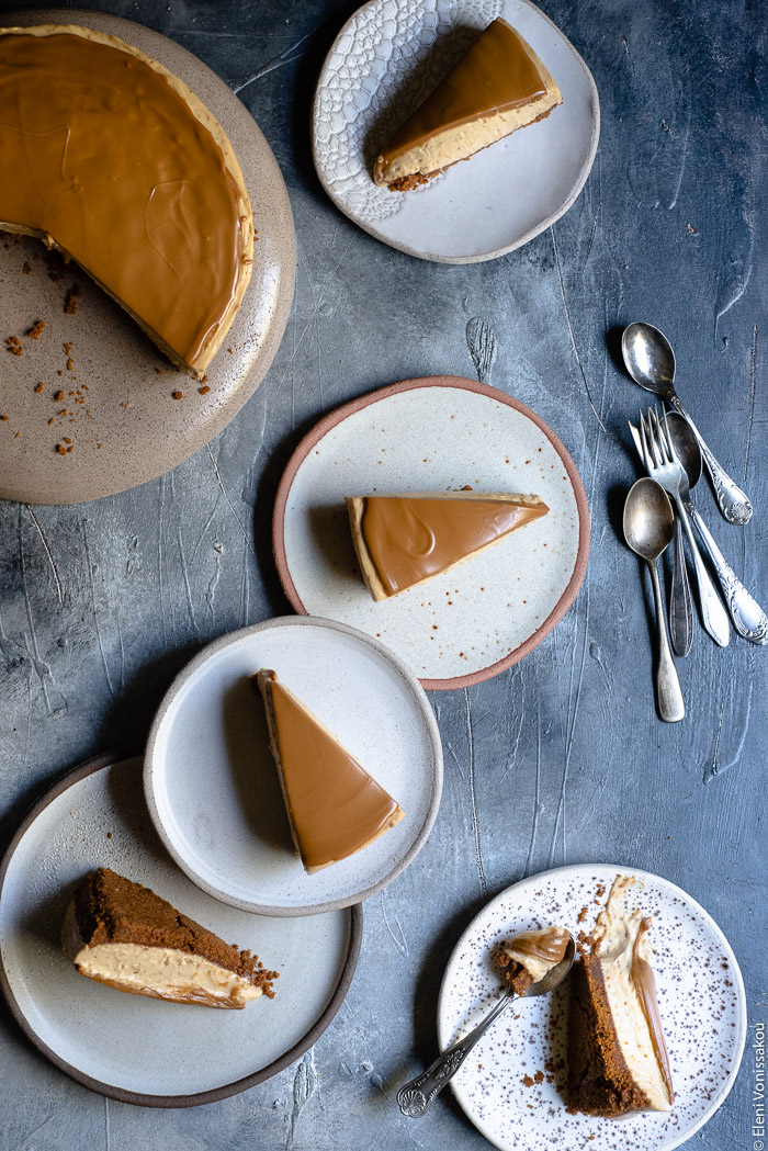 Easy Speculoos Cheesecake www.thefoodiecorner.gr Photo description: Five small plates with slices of speculoos cheesecake on them, arranged on a colourful surface. Some spoons lie to the right of the plates and in the top left corner is the cut cheesecake, half visible.