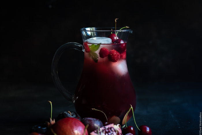 Pomegranate and Sour Cherry Rosé Sangria www.thefoodiecorner.gr Photo description: A close side view of a jug containing sangria, ice cubes, mint, cherries and raspberries.