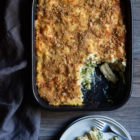 Broccoli Cheese Pasta Bake www.thefoodiecorner.gr Photo description: Top view of a baking dish with broccoli cheese pasta bake. One piece from the bottom right corner is missing. To the bottom of the dish is a small plate with the piece of pasta bake and a fork on it.