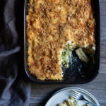 Broccoli Cheese Pasta Bake www.thefoodiecorner.gr Photo description: Top view of a baking dish with broccoli cheese pasta bake. One piece from the bottom right corner is missing. To the bottom of the dish is a small plate with the piece of pasta bake and a fork on it.