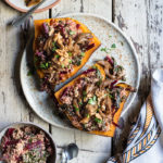 Slow Cooker BBQ Pulled Oyster Mushrooms over Beet Greens Millet and Sweet Potato www.thefoodiecorner.gr Photo description: A large plate with two sweet potatoes on it, topped with millet and pulled mushrooms. To the top of the photo two smaller plates, one with mushrooms and another with parsley and walnuts for garnishing. To the bottom of the photo a bunched up tea towel and a small bowl with beet greens millet.