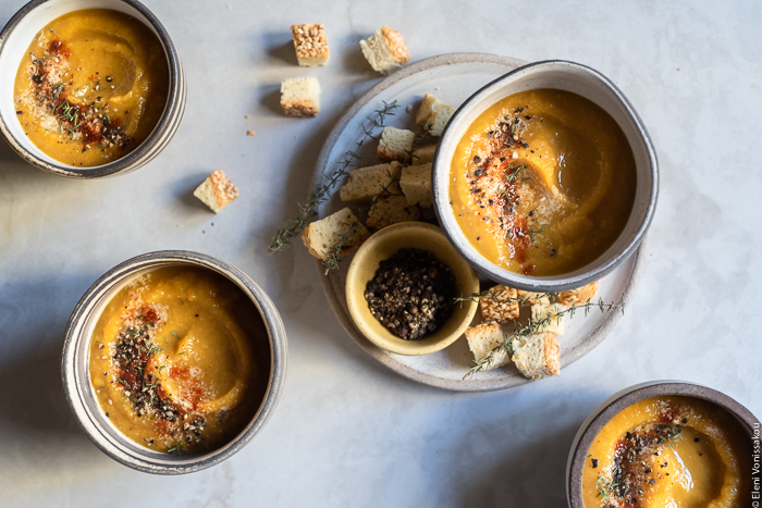 Slow Cooker Butternut Squash and Red Lentil Soup - Low Waste and Minimal Prep www.thefoodiecorner.gr Photo description: Four small bowls of soup arranged on a marble surface. One of the bowls is on a small plate along with a tiny bowl of black pepper and some croutons. The soup in the bowls is garnished with black pepper, paprika and nutritional yeast. 