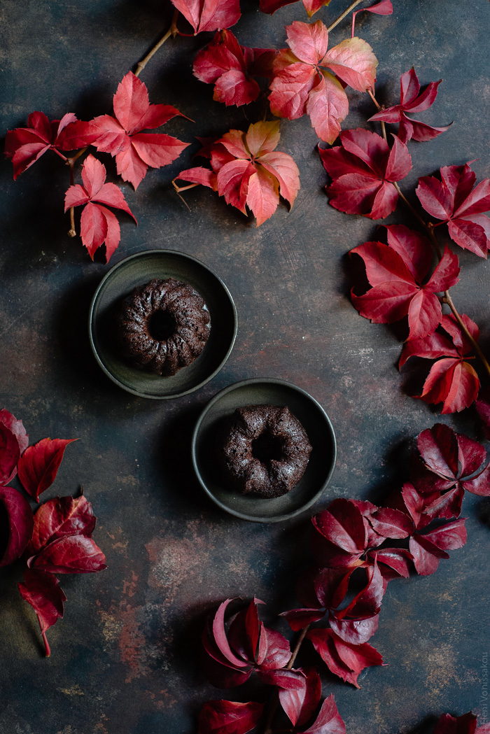 Chocolate and Beetroot Mini Bundt Cakes with a Quick Ganache (Plant Based) www.thefoodiecorner.gr Photo description: Two small plates each with a mini budnt cake on top. Surrounding the plates are lots of pretty autumn leaves.