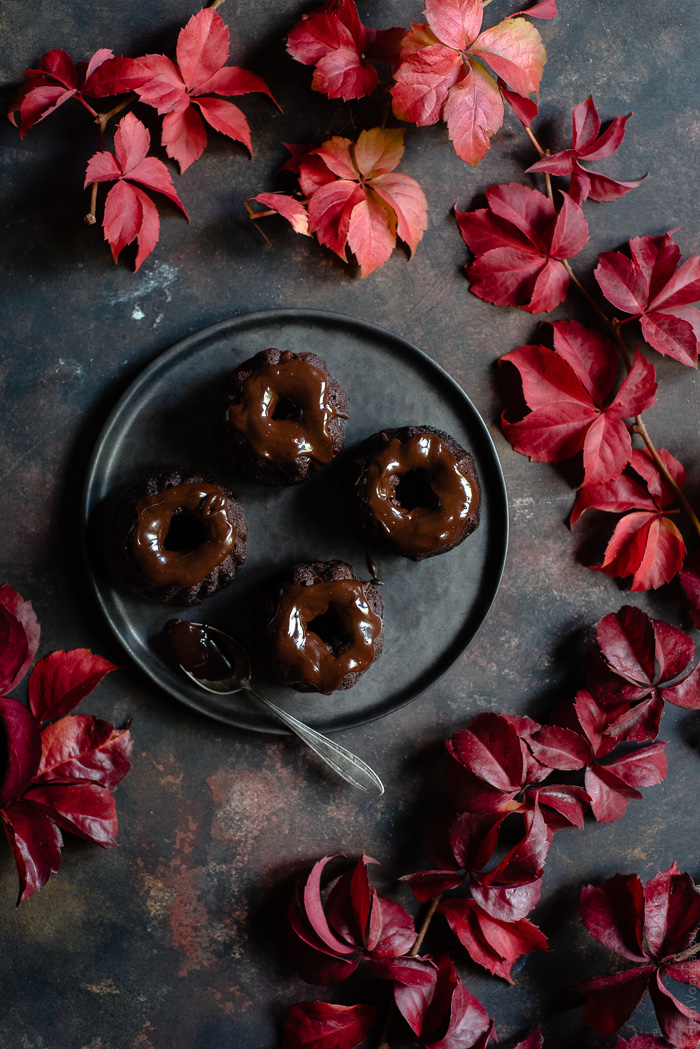 Chocolate and Beetroot Mini Bundt Cakes with a Quick Ganache (Plant Based) www.thefoodiecorner.gr Photo description: A plate of mini bundt cakes with a ganache topping. Surrounding the plate are lots of pretty autumn leaves.