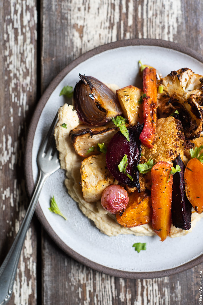 Cumin Roasted Root Vegetable Medley. My Winter “Briam”. www.thefoodiecorner.gr Photo description: A close view of a small ceramic plate with a portion of hummus and roasted vegetables. To the left of the food, lying on the plate, is a fork with some hummus on it.