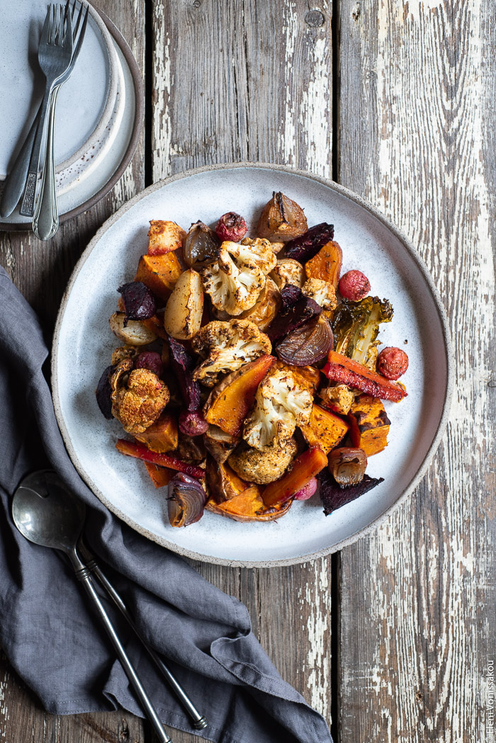 Cumin Roasted Root Vegetable Medley. My Winter “Briam”. www.thefoodiecorner.gr Photo description: A ceramic dish full of roasted root vegetables. To the top left of the dish are some empty plates and forks, half visible. To the left of the dish is a linen napkin and some serving spoons.