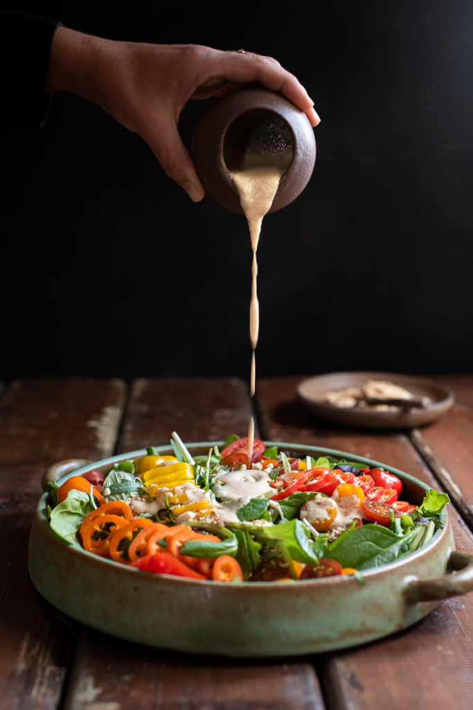 Cherry Tomato and Mini Sweet Pepper Green Salad with Tahini Sauce and Dukkah www.thefoodiecorner.gr Photo description: side view of a large dish with salad and hand pouring sauce over the top.