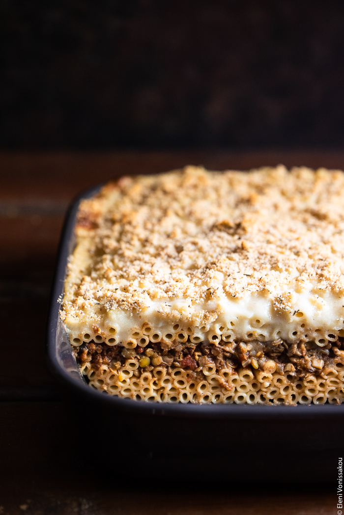 Pastitsio (Greek Pasta Bake) with Lentil and Mushroom Sauce, and Oat Milk Bechamel www.thefoodiecorner.gr Photo description: A ¾ view of the baking dish with the cooked pastitsio. A few slices are missing so one can see the layers of pasta and lentil sauce inside the dish.