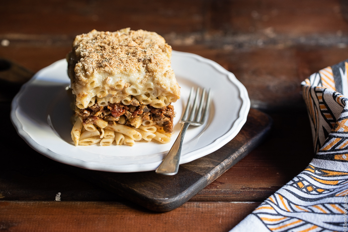 Pastitsio (Greek Pasta Bake) with Lentil and Mushroom Sauce, and Oat Milk Bechamel www.thefoodiecorner.gr Photo description: A slice of pastitsio on a pretty plate sitting on a chopping board. A fork lies next to the slice on the plate. 