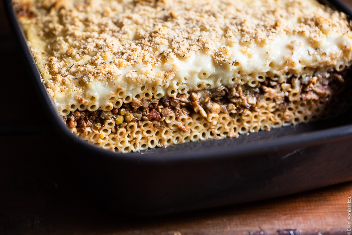 Pastitsio (Greek Pasta Bake) with Lentil and Mushroom Sauce, and Oat Milk Bechamel www.thefoodiecorner.gr Photo description: A closer ¾ view of the baking dish with the cooked pastitsio. A few slices are missing so one can see the layers of pasta and lentil sauce inside the dish.