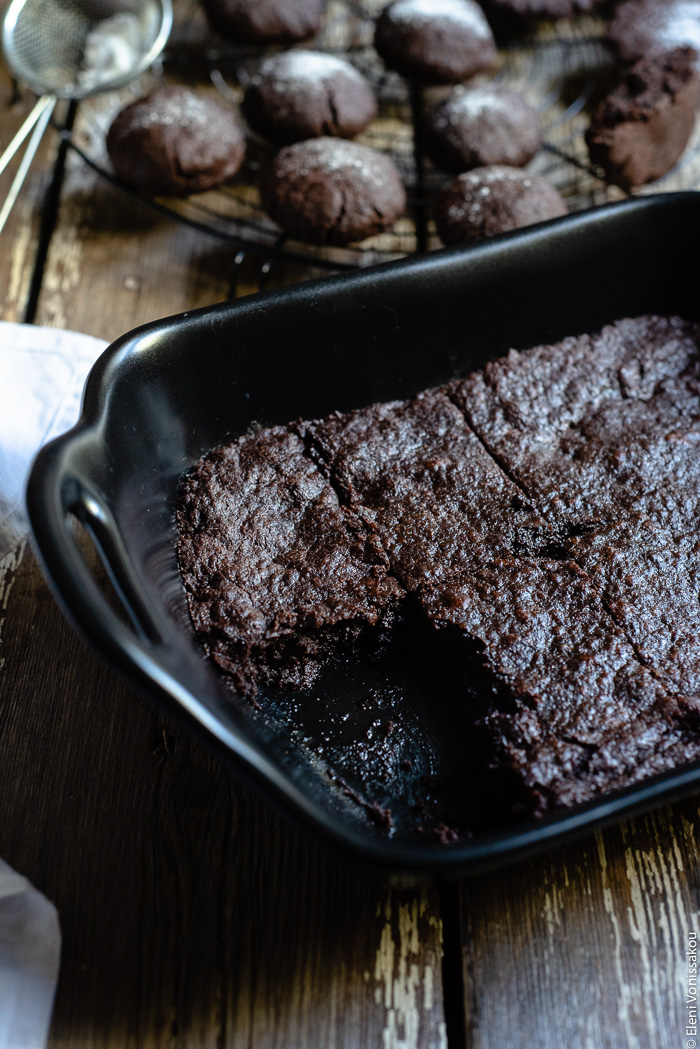 Chocolate Tahini Olive Oil Cookies or Brownies (One Recipe, Two Treats) www.thefoodiecorner.gr Photo description: A baking dish with brownies, the piece to the front of the photo having been removed. In the background a cooling rack with biscuits/cookies on it.