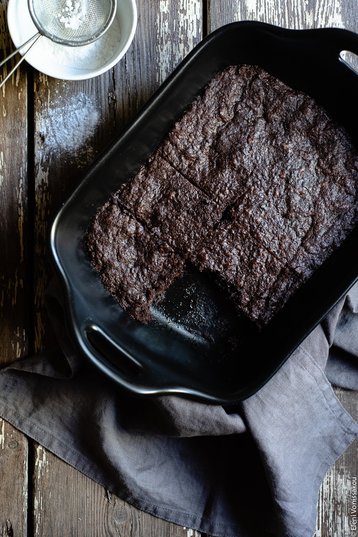 Chocolate Tahini Olive Oil Cookies or Brownies (One Recipe, Two Treats) www.thefoodiecorner.gr Photo description: A top view of a baking dish with brownies, one of them missing. Underneath there is a bunched up linen napkin. To the top of the photo a small bowl with icing sugar.