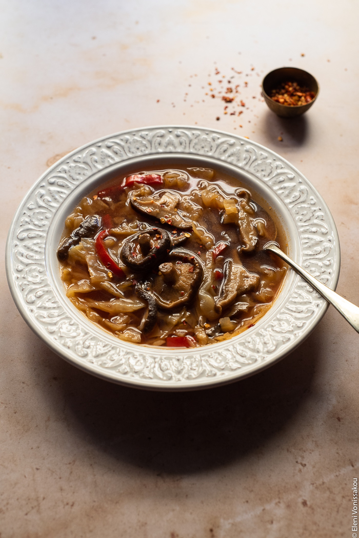 Slow Cooker Hot and Sour Cabbage Soup with Shiitake Mushrooms www.thefoodiecorner.gr Photo description: A close, ¾ view of a bowl of soup with a spoon in it, the backlighting making the surface of the liquid slightly shiny.