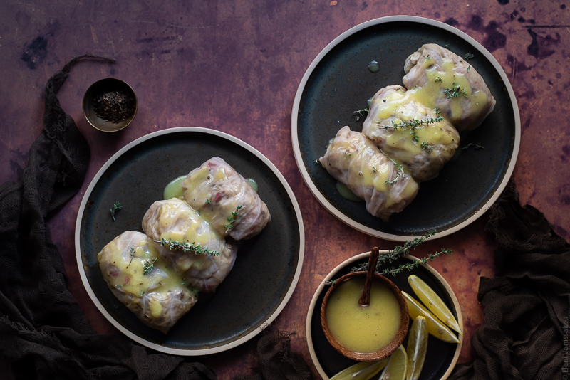 Shiitake, Rice and Truffle Oil Stuffed Cabbage Rolls with Lemon Vinaigrette www.thefoodiecorner.gr Photo descriptions: Two plates each with three stuffed cabbage rolls drizzled with sauce. To the bottom of the image is a small plate with lemon slices and a little bowl of lemon sauce.