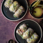 Shiitake, Rice and Truffle Oil Stuffed Cabbage Rolls with Lemon Vinaigrette www.thefoodiecorner.gr Photo description: Two plates with stuffed cabbage rolls on a rusty coloured surface. One of the rolls is cut showing the rice stuffing inside. In the top right corner of the image is a small plate with slices of lemon and a small bowl of vinaigrette.