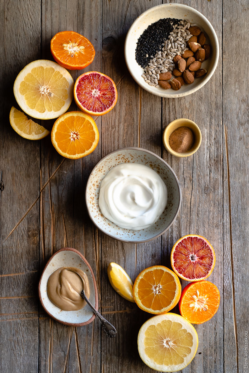 Acerola and Coconut Yoghurt Citrus Fruit Platter www.thefoodiecorner.gr Photo description: Some halved citrus fruit arranged on a distressed wooden surface. In the middle is a bowl of coconut yoghurt. To the top right of the photo is a small dish with nuts and seeds. To the bottom left is a small plate with peanut butter and a spoon.