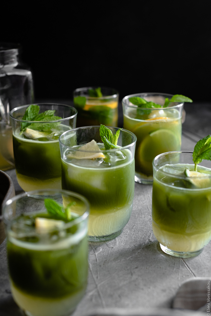 Σπιτική Λεμονάδα με Τσάι Matcha www.thefoodiecorner.gr Photo description: A close up view of some glasses of matcha lemonade, their two layers visible (lemonade at the bottom and matcha sitting on top). The drinks are garnished with small wedges of lemon and lime and some spearmint leaves.