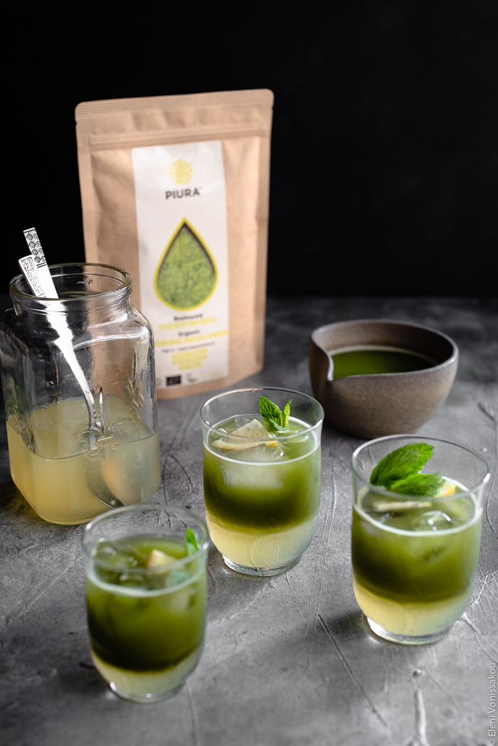 Easy Homemade Matcha Lemonade www.thefoodiecorner.gr Photo description: A 3/4 view of three glasses of matcha lemonade, their two layers visible (lemonade at the bottom and matcha sitting on top). Behind them are a jug of matcha, a jar of lemonade concentrate and a packet of Piura matcha powder.