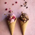 Four Ingredient Banana Ice Cream - Raspberry or Chocolate www.thefoodiecorner.gr Photo description: Two cones filled with ice cream, one raspberry one chocolate flavoured. Both have some toppings sprinkled on, raspberries, chopped chocolate and some chopped granola bar. The ice creams are lying on a colourful pink surface.