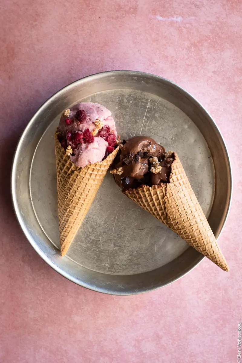 Four Ingredient Banana Ice Cream - Raspberry or Chocolate www.thefoodiecorner.gr Photo description: A round metal cake tin on a pink surface. In the tin are two cones filled with ice cream, one raspberry and one chocolate, each sprinkled with extra raspberries and chopped chocolate.