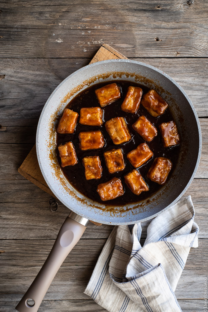 Fried Silken Tofu with Honey Garlic Sauce www.thefoodiecorner.gr Photo description: A frying pan with pieces of tofu in a dark garlic honey sauce. Near the handle is a linen napkin.