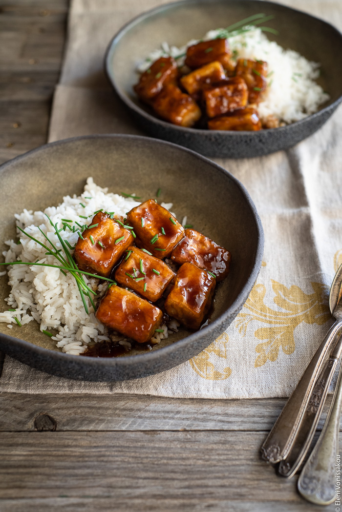 Fried Silken Tofu with Honey Garlic Sauce www.thefoodiecorner.gr Photo description: A ¾ view of two ceramic bowls with rice and honey garlic tofu. The bowls are sitting on a linen tea towel with a vintage spoon and fork in one corner.