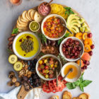 Bruschetta Board with Pickled Cherries, Marinated Cherry Tomatoes, Apricot Salsa and Olive Oil Dip www.thefoodiecorner.gr Photo description: A large wooden board full of tasty bruschetta toppings, fruit, tomatoes, honey, nuts, avocado, pesto and crackers. Around the board are some toasted slices of bread, a linen napkin and three glasses of rose wine.