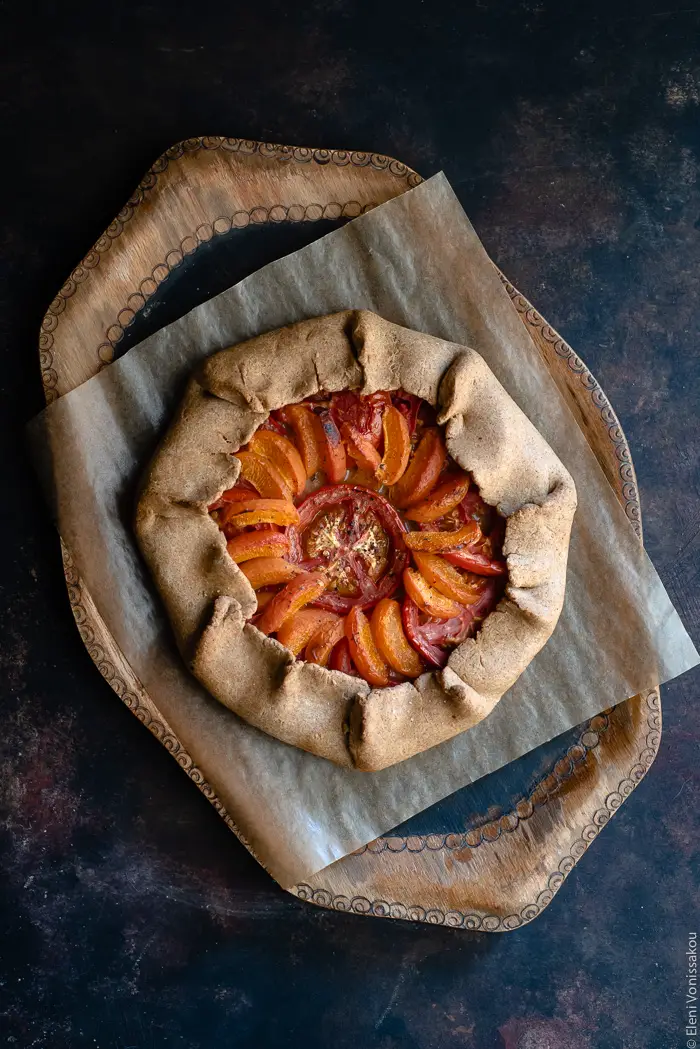 Apricot and Tomato Spelt Galette with Basil Vinaigrette www.thefoodiecorner.gr Photo description: A full galette with apricot and tomato slices arranged nicely inside. The galette is sitting on a piece of brown grease-proof paper which is in turn on a wooden tray.