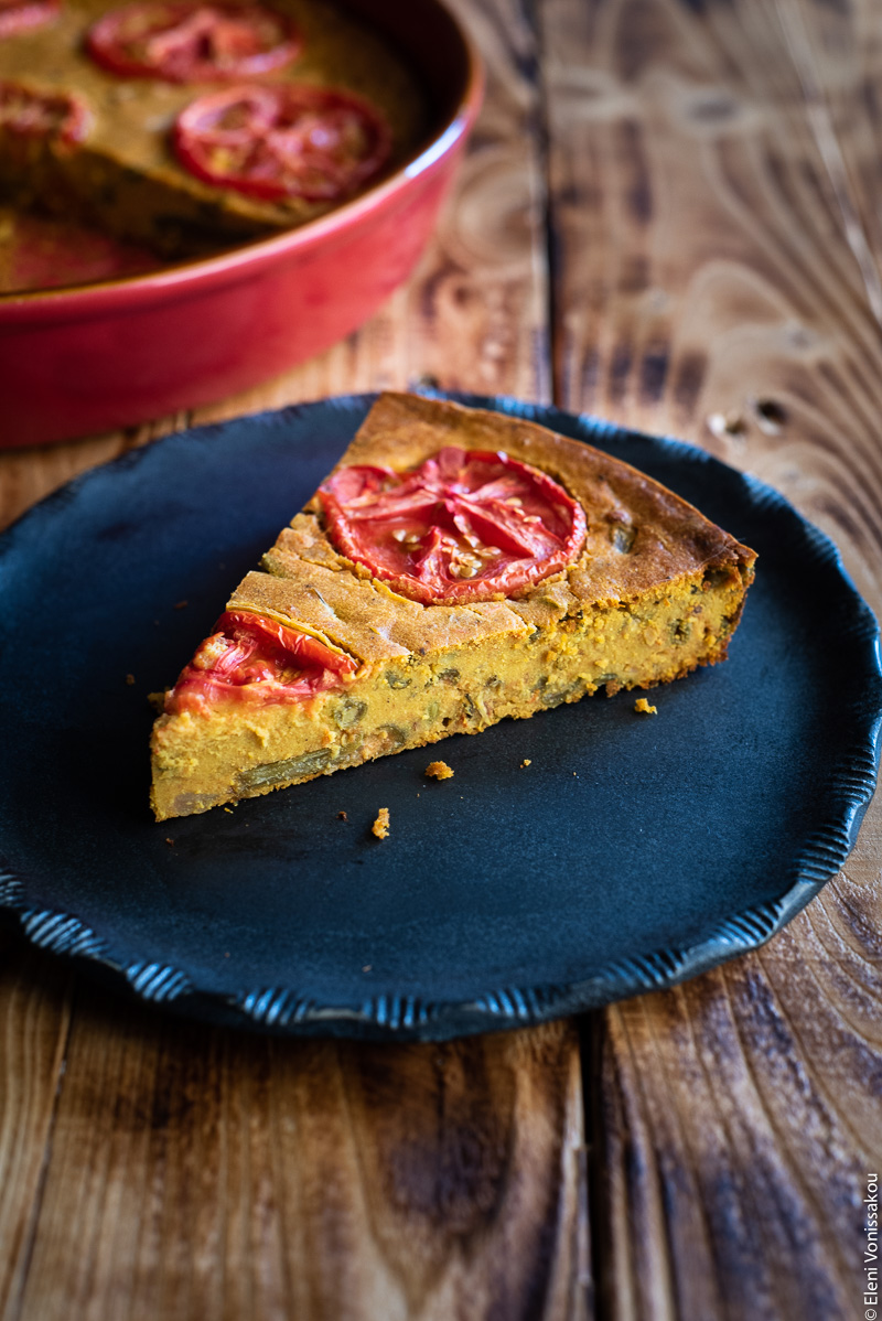 Chickpea Flour Pie (aka Plant-Based Frittata) with Leftover Green Bean Stew www.thefoodiecorner.gr Photo description: A black ceramic plate with a pretty pattern around the edge, and a slice of chickpea flour pie on it. The pie is decorated with slices of tomato on top which have cooked down while baking.