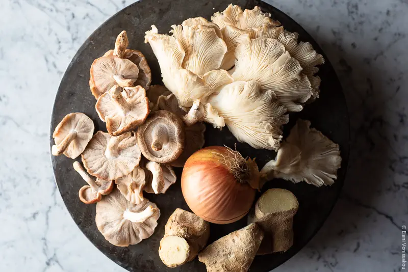 Μανιταρόσουπα με Ζυμαρικά, Εμπνευσμένη από την Βιετναμέζικη Σούπα Pho www.thefooodiecorner.gr Photo description: Some fresh mushrooms, an onion and two pieces of ginger on a round metal surface.
